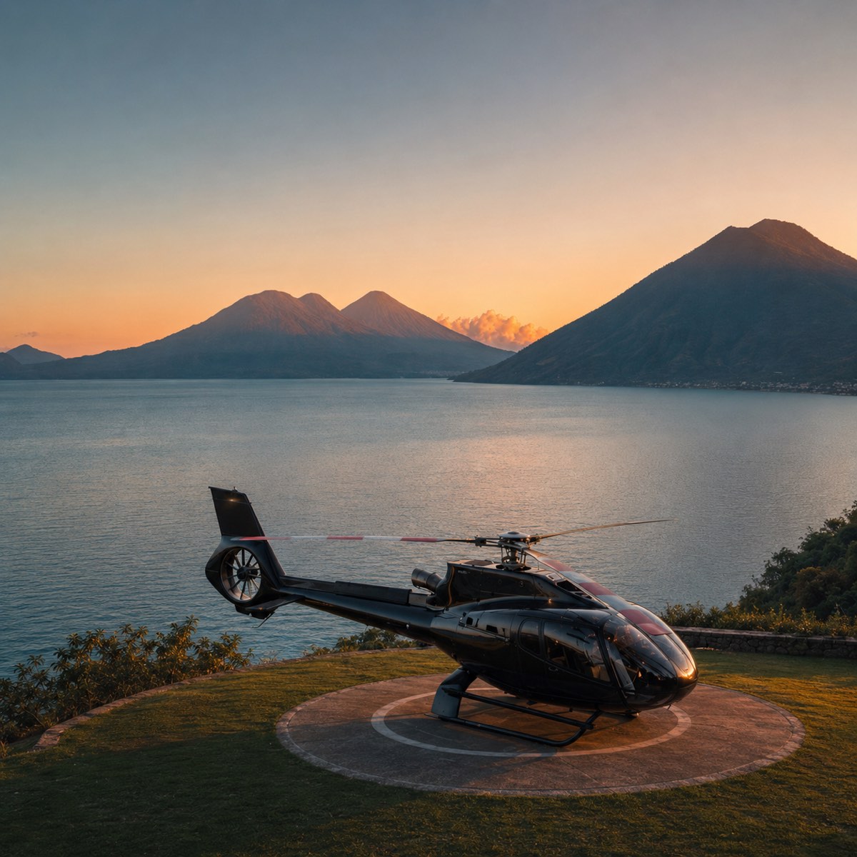 A private helicopter on a helipad overlooking Lake Atitlán at sunset, with the volcanoes behind