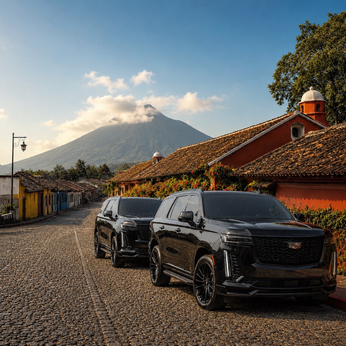 Black executive SUVs parked on a cobblestone street in Antigua Guatemala, with the volcano behind